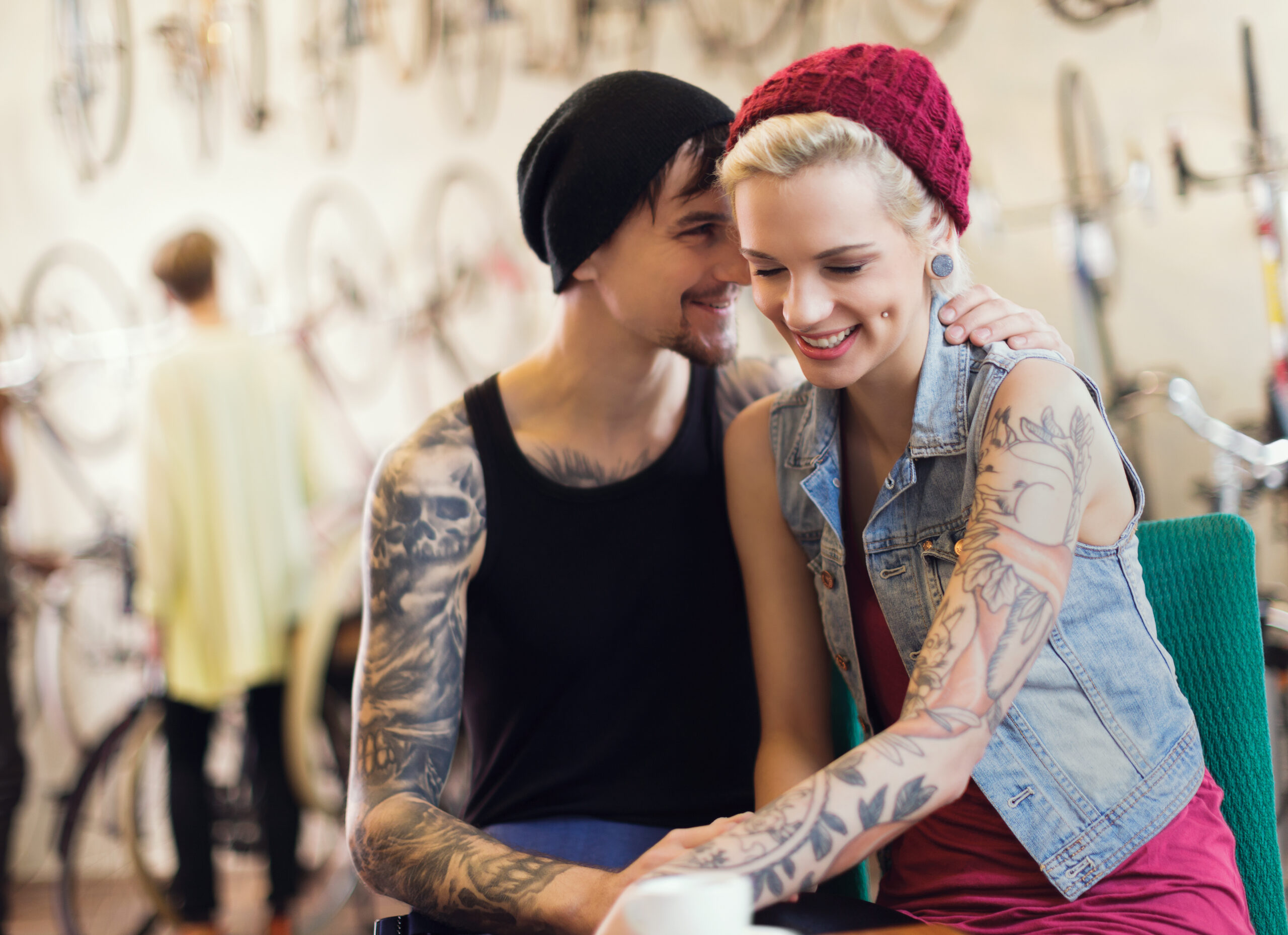 Young tatooed owners of an antique bike store in Berlin, Germany. Owners are sitting in the foreground while a customer looks at bikes in the background. Horizontal shot.